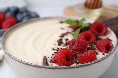 Photo of Tasty cooked semolina porridge with raspberries, chocolate and mint on table, closeup