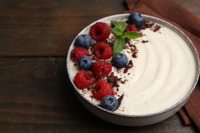 Photo of Tasty cooked semolina porridge with berries, chocolate and mint on wooden table, closeup. Space for text