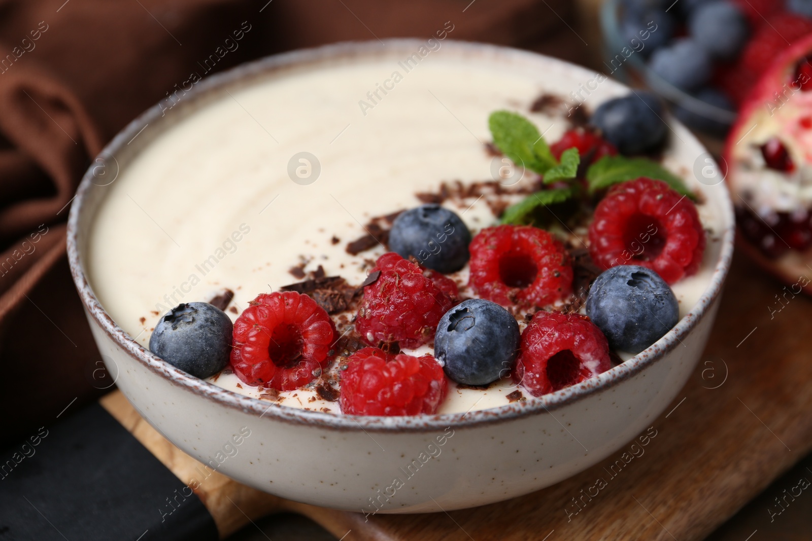 Photo of Tasty cooked semolina porridge with berries, chocolate and mint on table, closeup