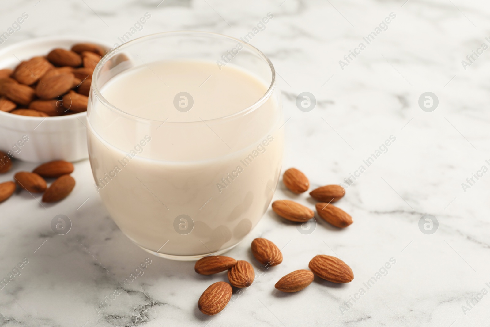 Photo of Glass of almond milk and nuts on white marble table, closeup. Space for text