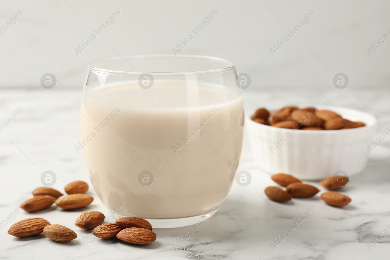 Photo of Glass of almond milk and nuts on white marble table, closeup