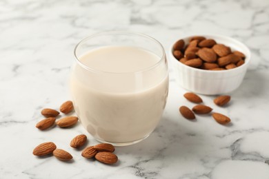 Photo of Glass of almond milk and nuts on white marble table, closeup