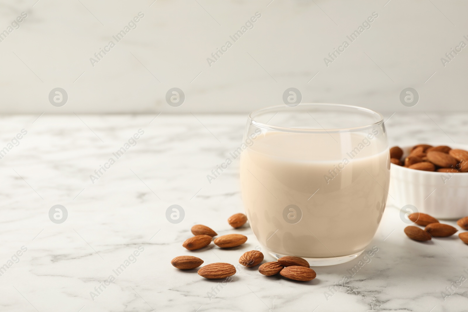 Photo of Glass of almond milk and nuts on white marble table, space for text