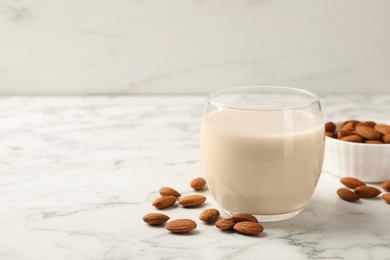 Photo of Glass of almond milk and nuts on white marble table, space for text