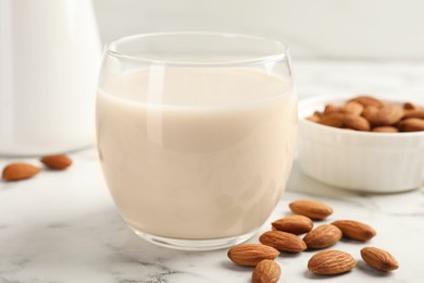 Glass of almond milk and nuts on white marble table, closeup