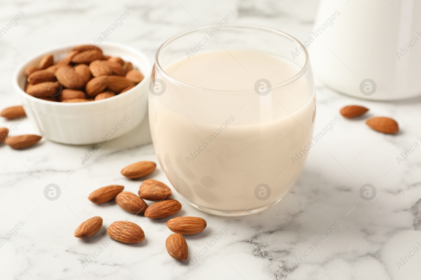 Photo of Glass of almond milk and nuts on white marble table, closeup