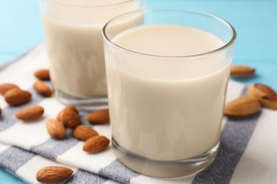 Photo of Glasses of almond milk and nuts on blue table, closeup