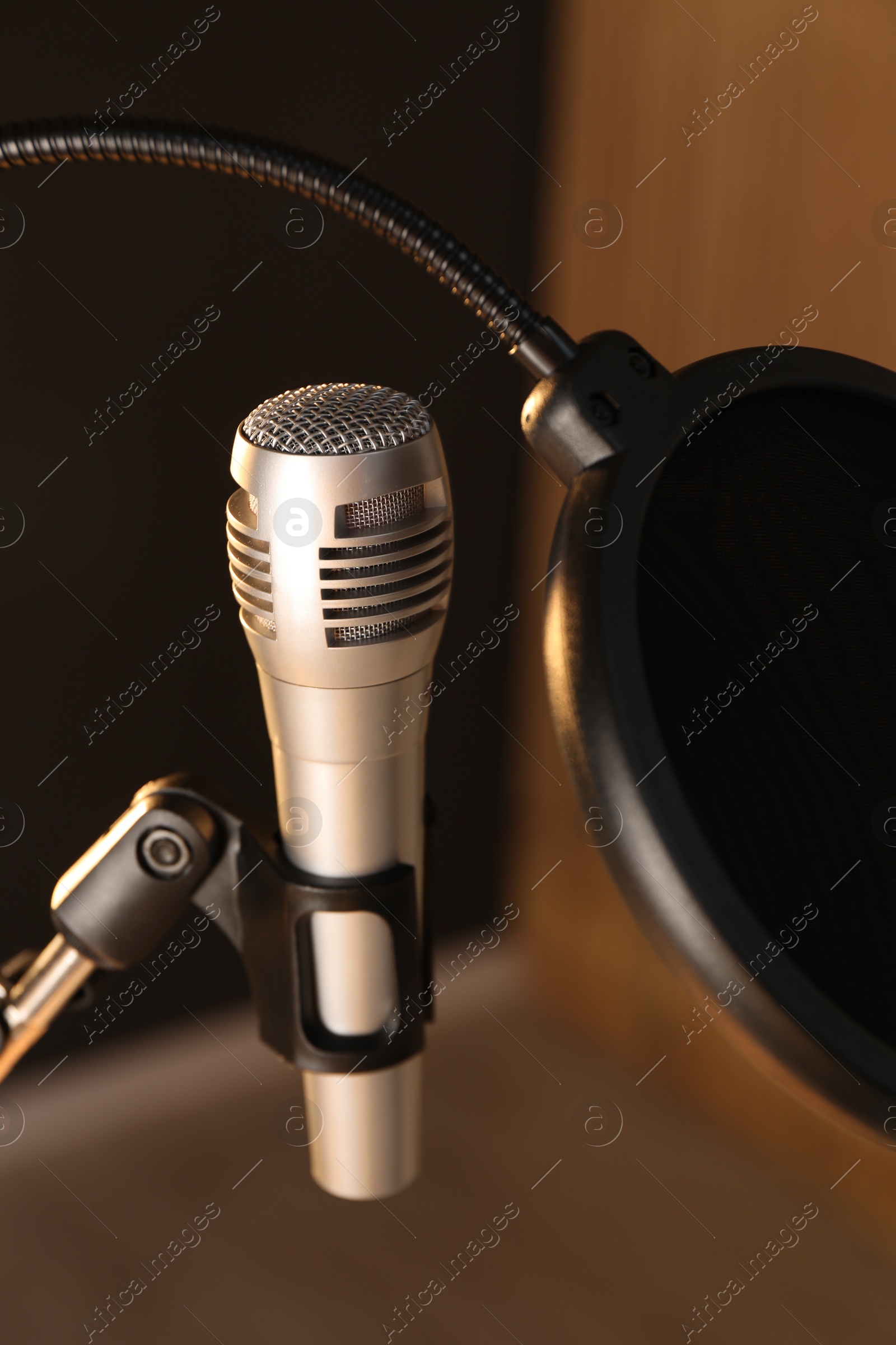 Photo of Stand with microphone and pop filter on blurred background, closeup. Sound recording and reinforcement