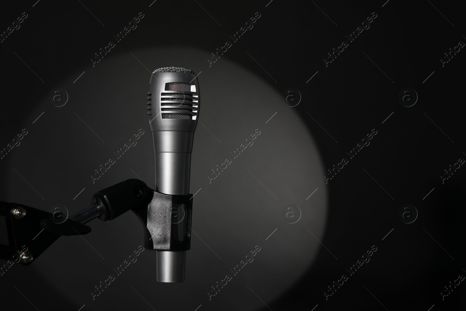 Photo of Stand with microphone in spotlight on black background, space for text. Sound recording and reinforcement