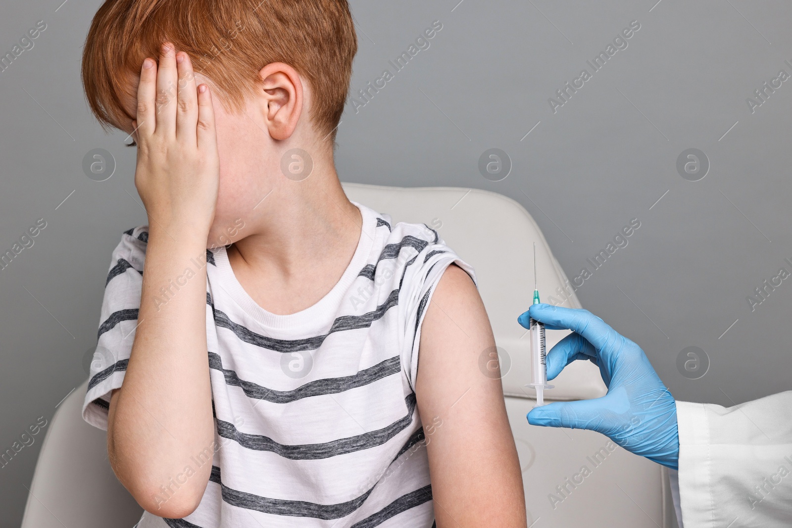 Photo of Dental phobia. Dentist with syringe near scared boy on grey background