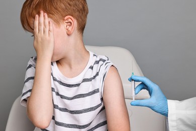 Dental phobia. Dentist with syringe near scared boy on grey background