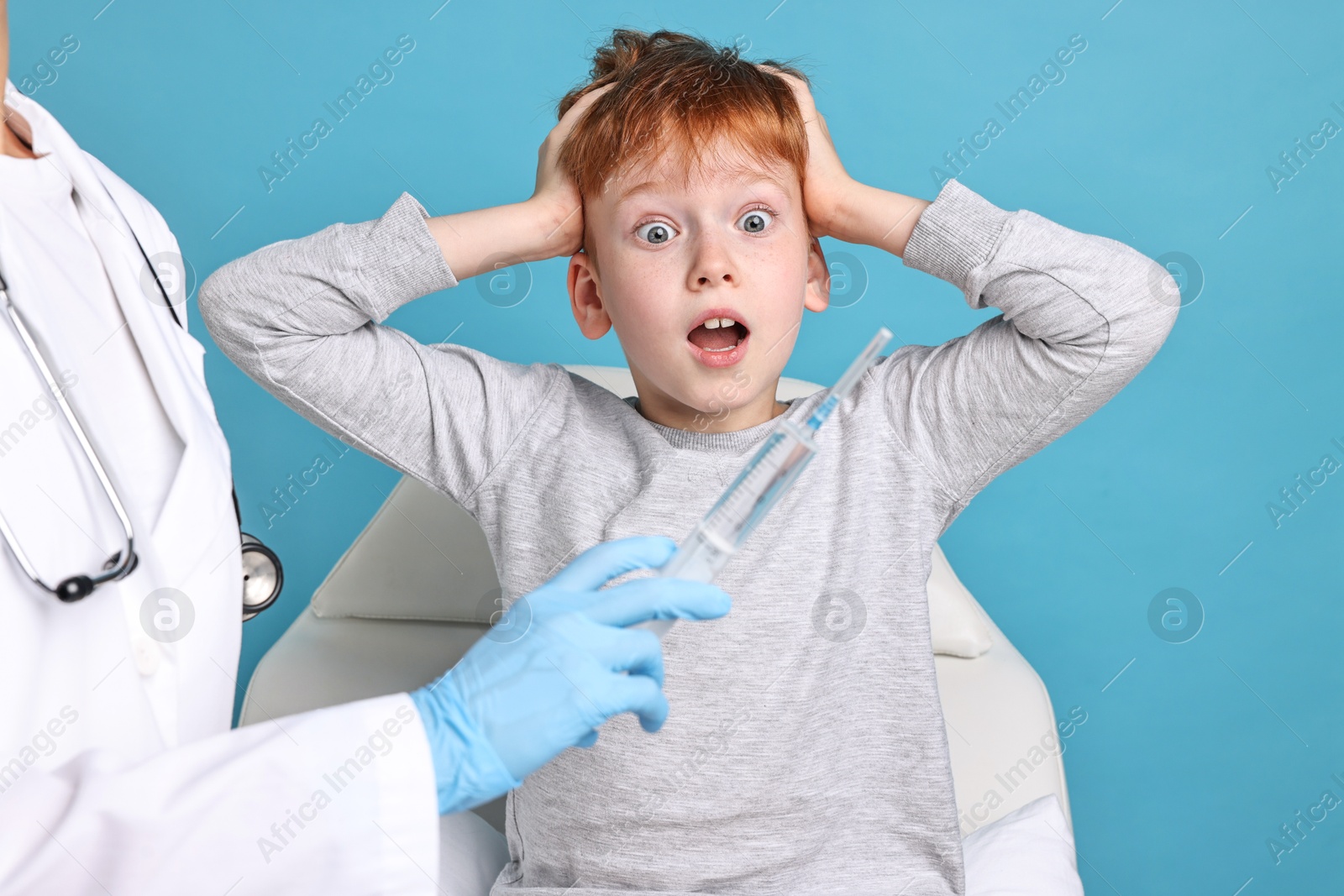 Photo of Dental phobia. Dentist with syringe near scared boy on light blue background