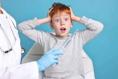 Dental phobia. Dentist with syringe near scared boy on light blue background