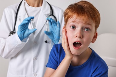 Photo of Dental phobia. Scared boy near dentist with syringe and vial on light grey background