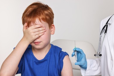 Dental phobia. Dentist with syringe near scared boy on light grey background