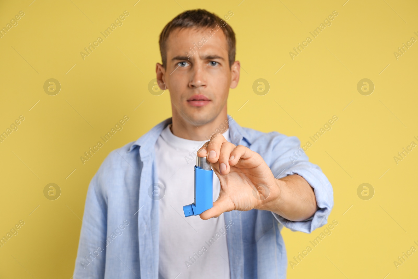 Photo of Man holding asthma inhaler on yellow background, selective focus