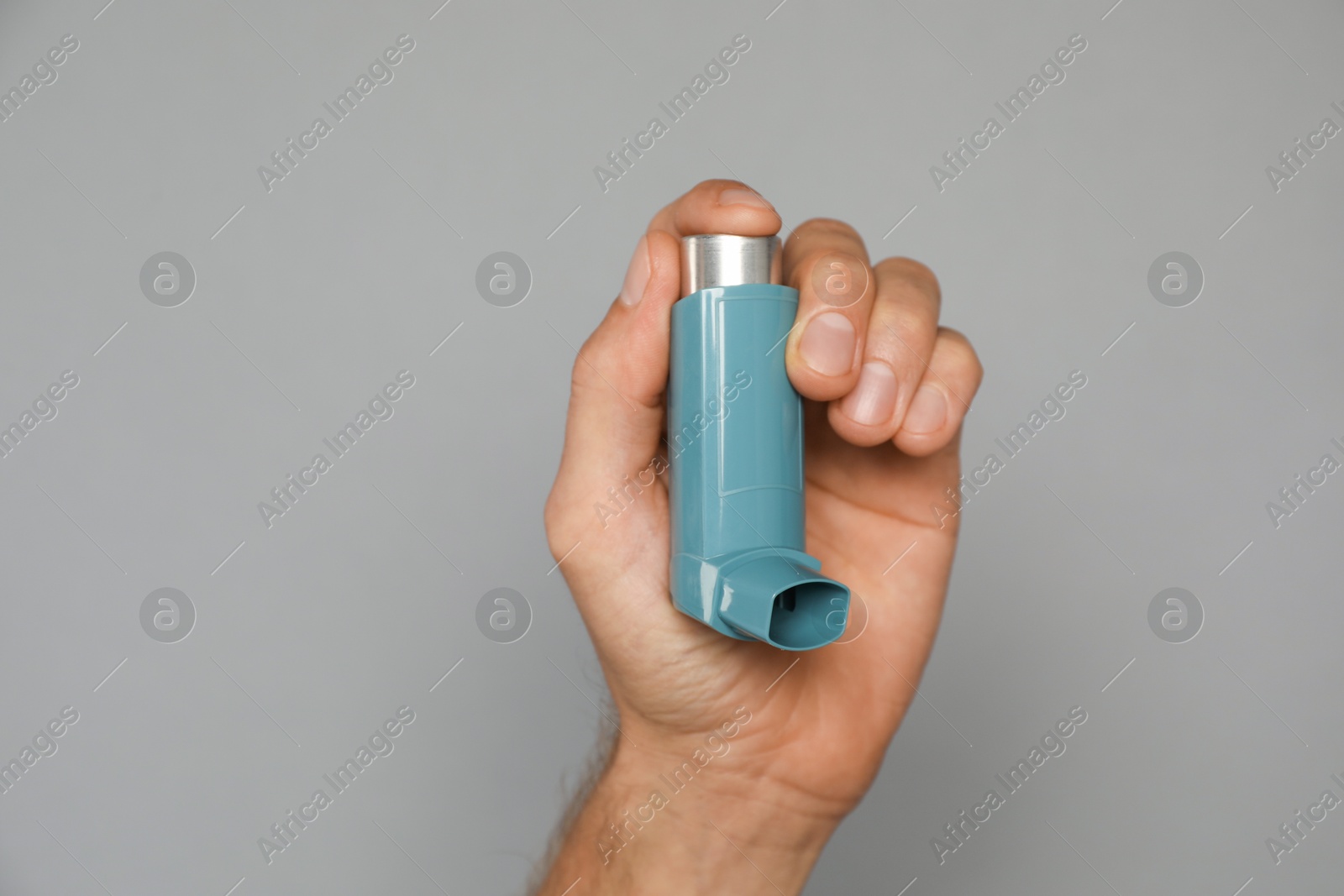 Photo of Man holding asthma inhaler on grey background, closeup