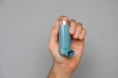 Photo of Man holding asthma inhaler on grey background, closeup