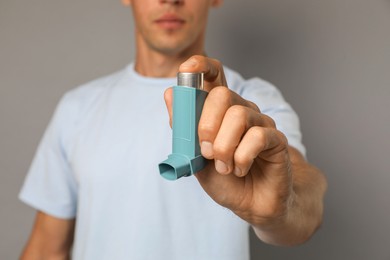 Man holding asthma inhaler on grey background, closeup