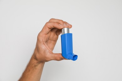 Photo of Man holding asthma inhaler on light background, closeup