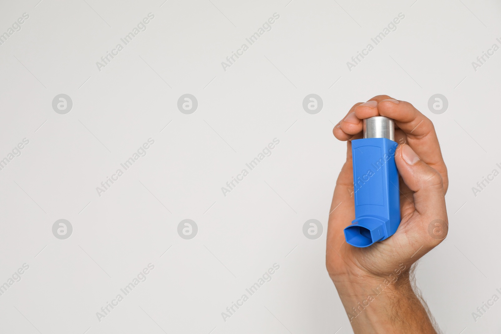 Photo of Man holding asthma inhaler on light background, closeup. Space for text