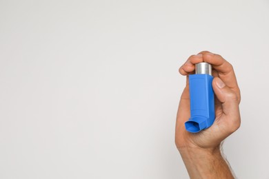 Photo of Man holding asthma inhaler on light background, closeup. Space for text