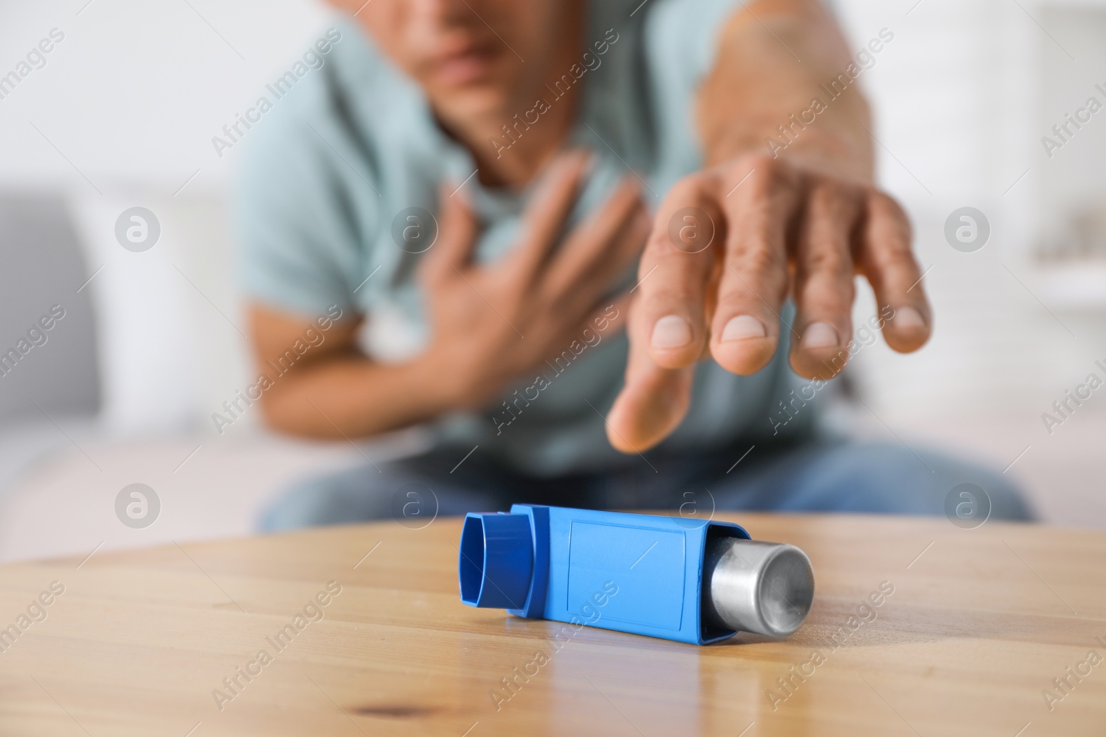 Photo of Man reaching for asthma inhaler at wooden table indoors, closeup