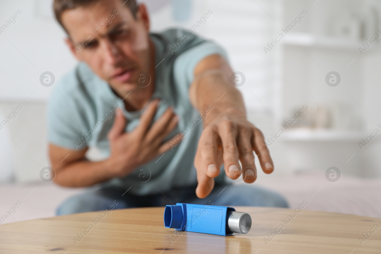 Photo of Man reaching for asthma inhaler at wooden table indoors, selective focus