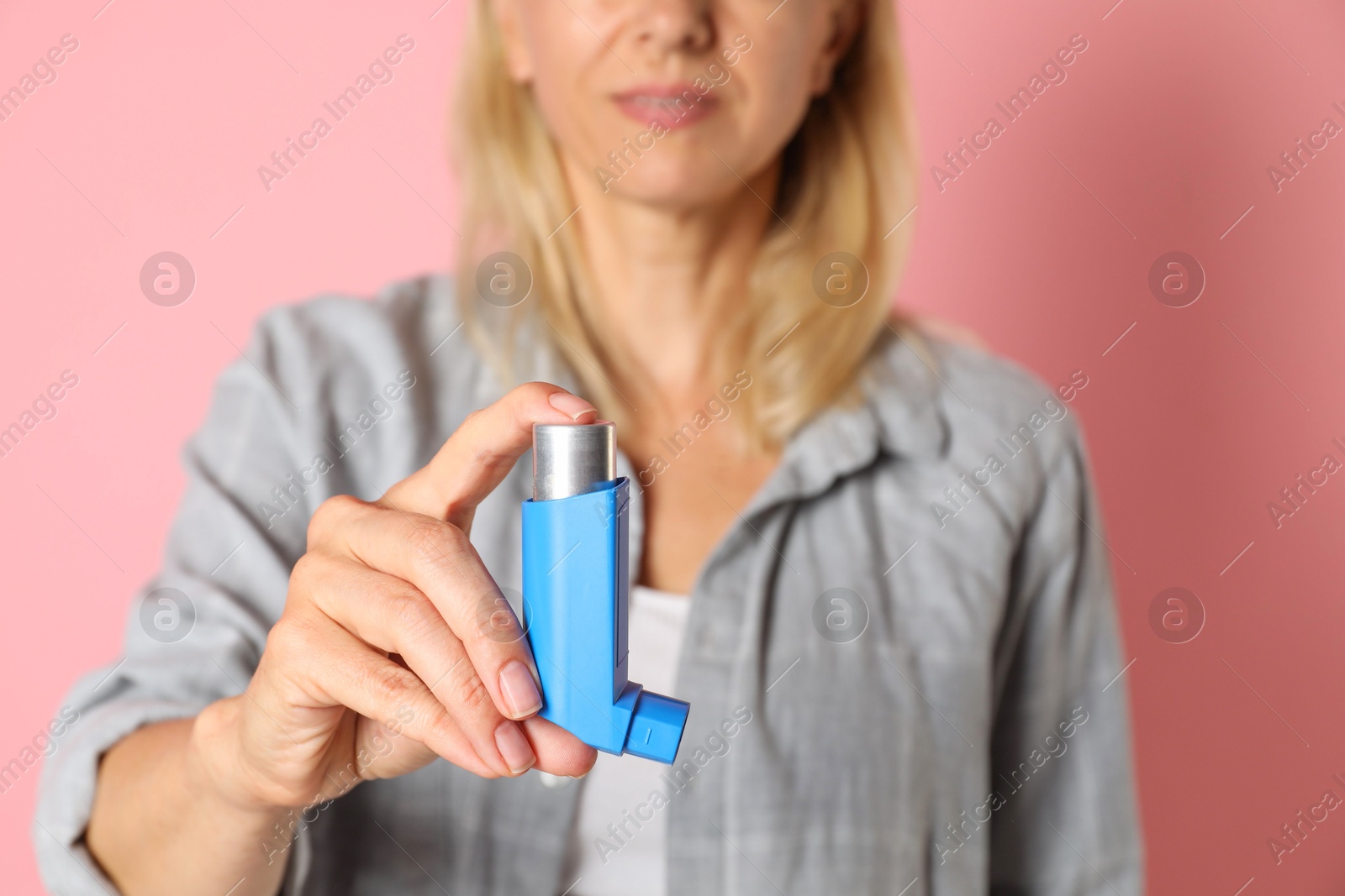 Photo of Woman holding asthma inhaler on pink background, closeup