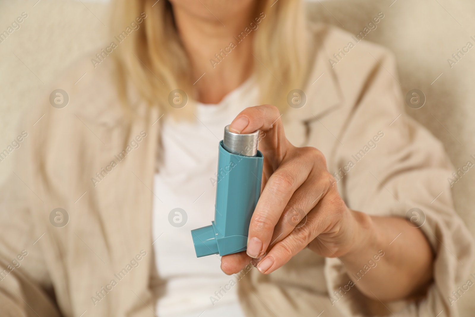 Photo of Woman holding asthma inhaler on beige background, closeup