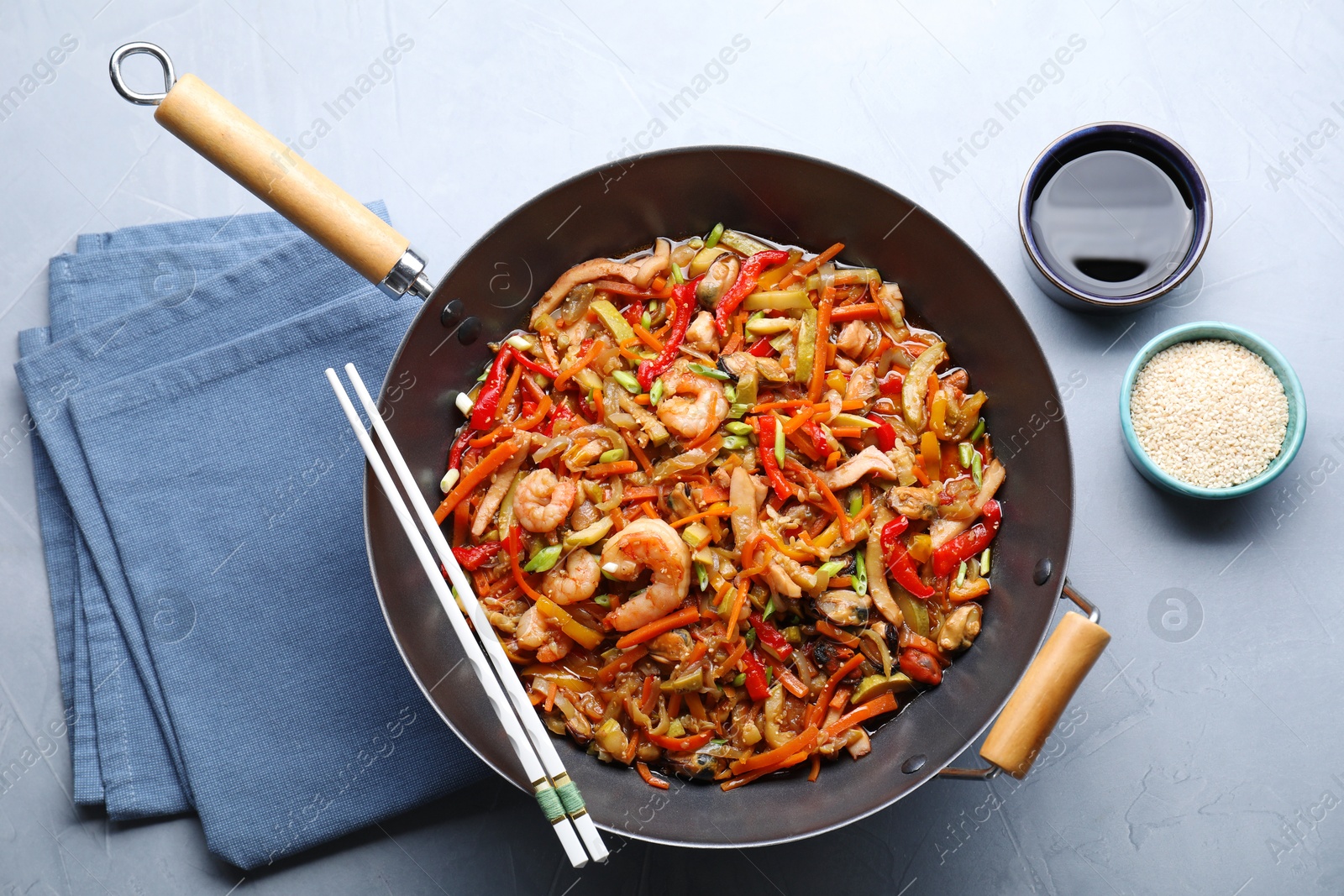 Photo of Stir-fry sea food in wok served on grey table, flat lay