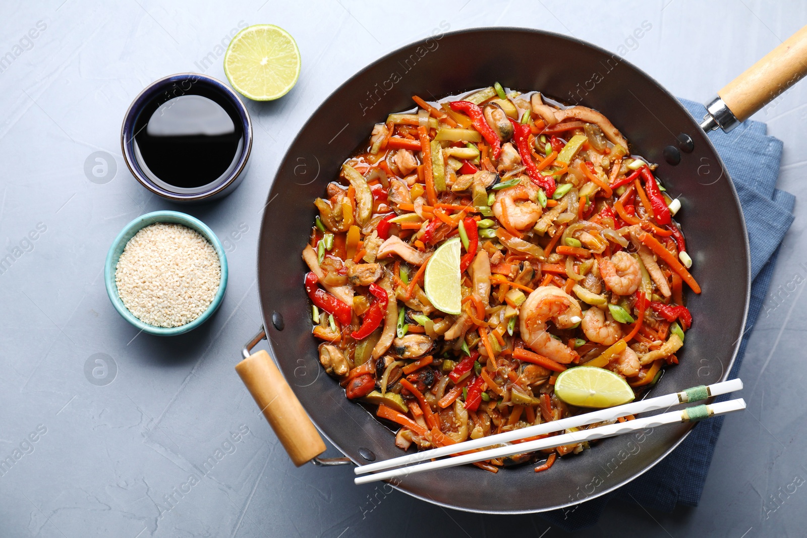 Photo of Stir-fry sea food in wok served on grey table, flat lay