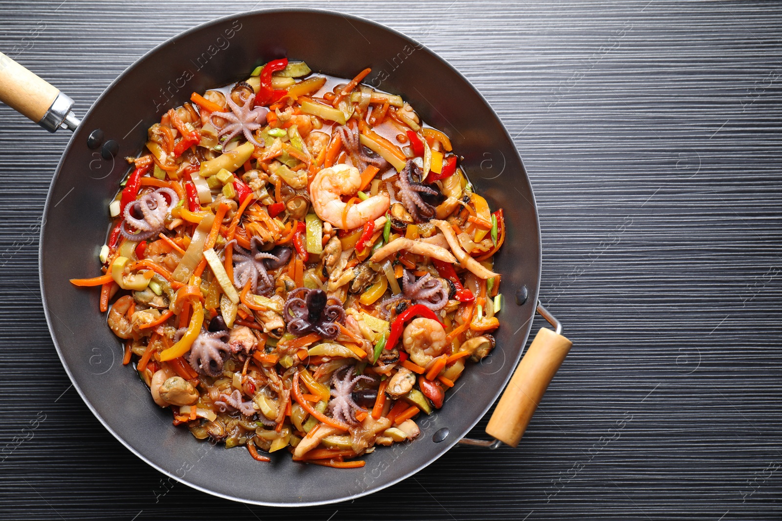 Photo of Stir-fry sea food in wok on black wooden table, top view. Space for text