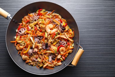 Photo of Stir-fry sea food in wok on black wooden table, top view. Space for text