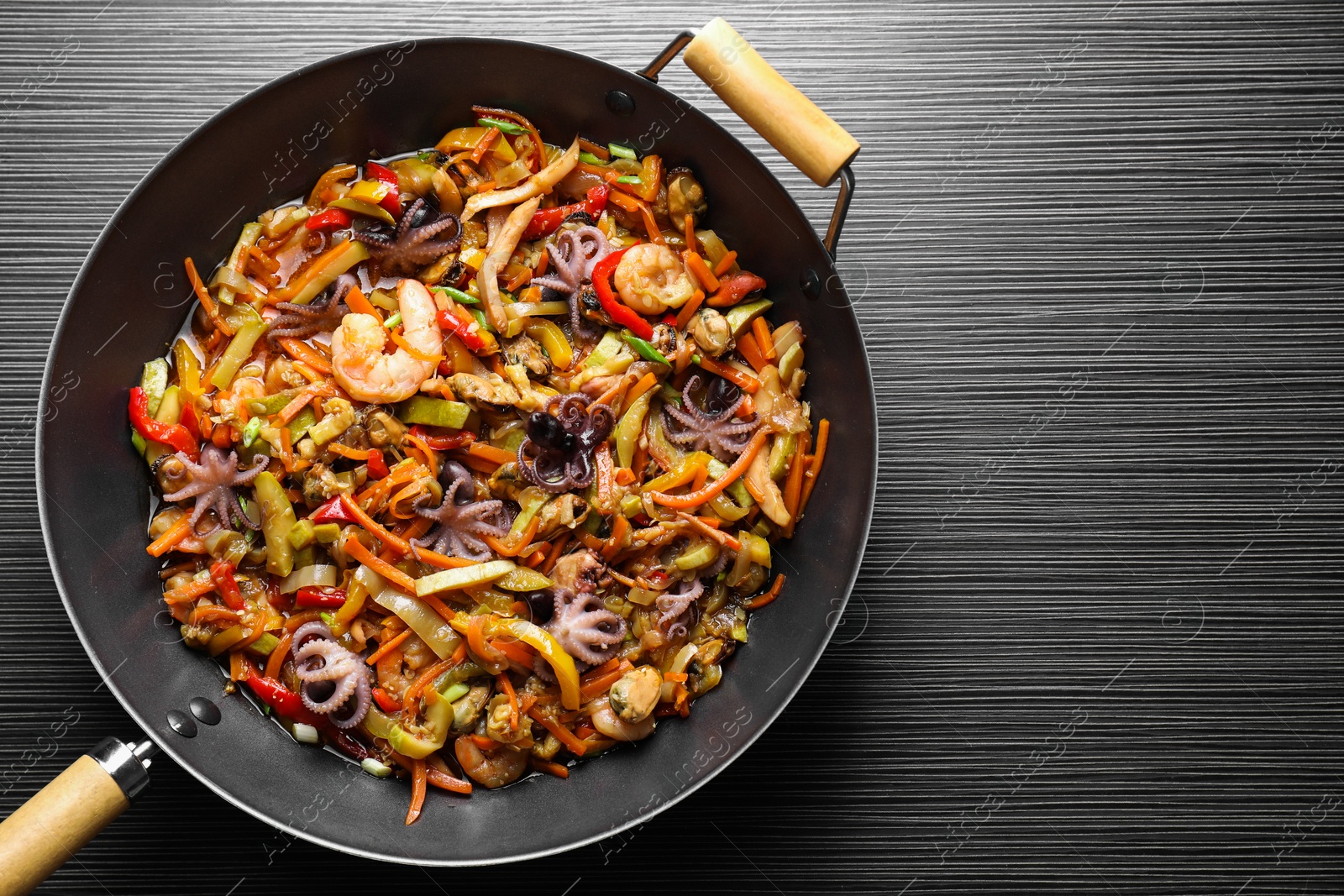 Photo of Stir-fry sea food in wok on black wooden table, top view. Space for text