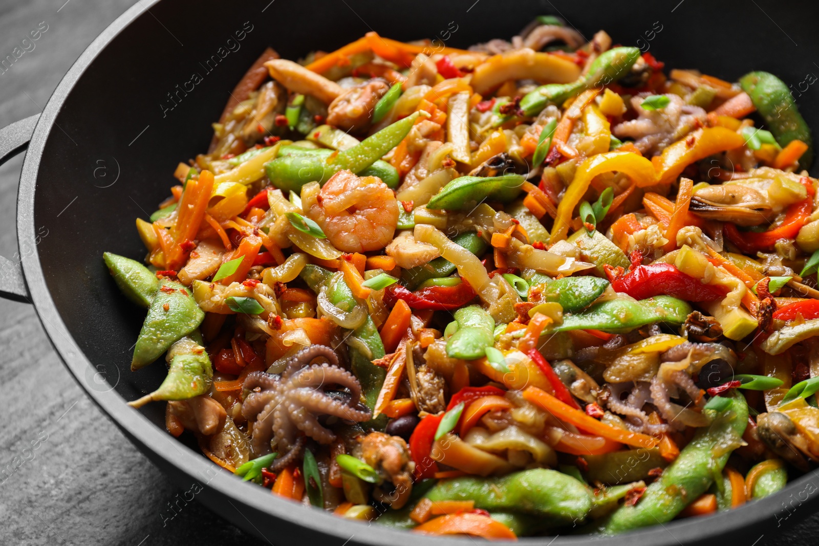 Photo of Stir-fry sea food in wok on grey table, closeup