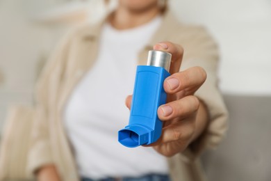 Woman holding inhaler indoors, closeup. Asthma treatment