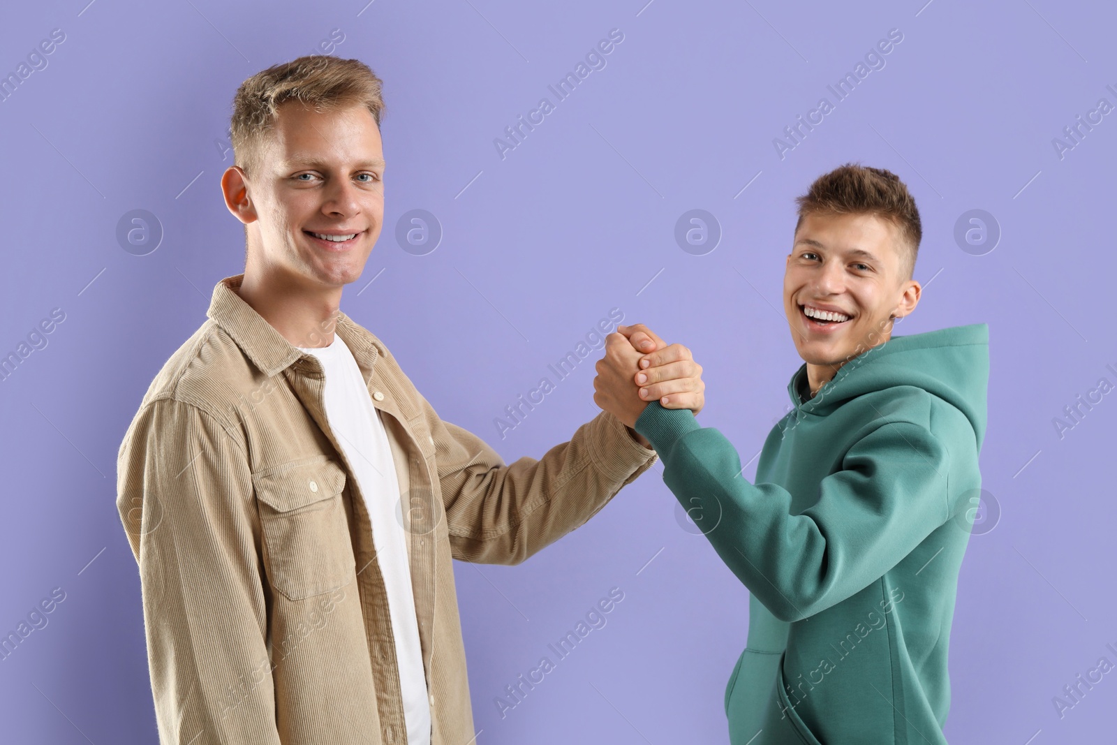 Photo of Happy brothers clasping hands on violet background