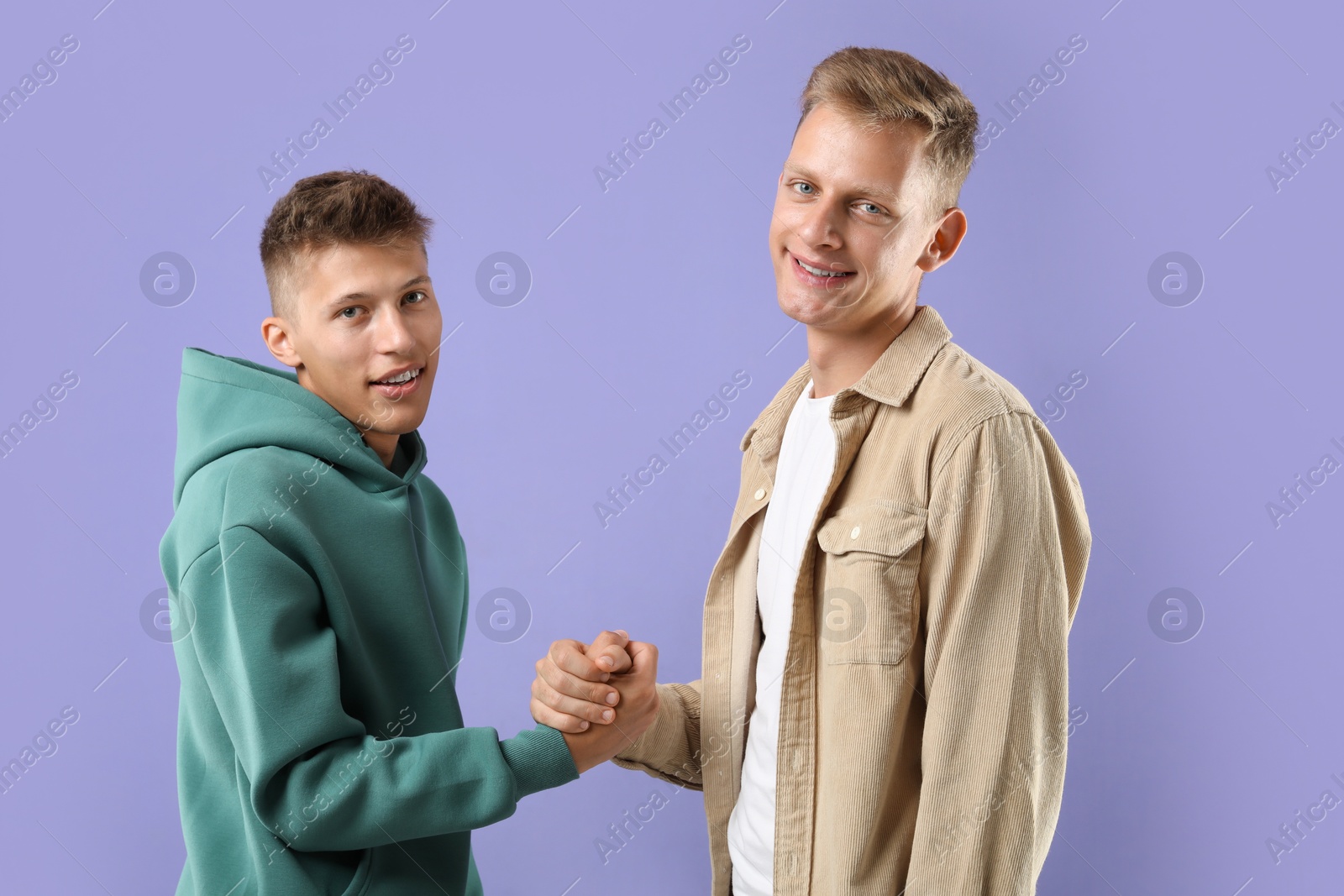 Photo of Happy brothers clasping hands on violet background