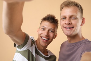 Happy brothers taking selfie on beige background