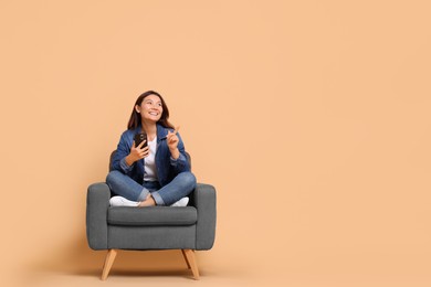 Photo of Smiling woman with smartphone sitting in armchair on beige background. Space for text