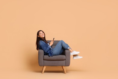 Photo of Smiling woman with smartphone sitting in armchair on beige background