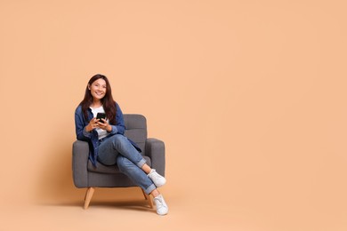 Photo of Smiling woman with smartphone sitting in armchair on beige background. Space for text