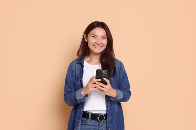 Photo of Smiling woman with smartphone on beige background