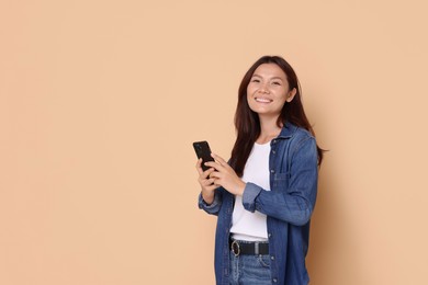 Photo of Smiling woman with smartphone on beige background. Space for text