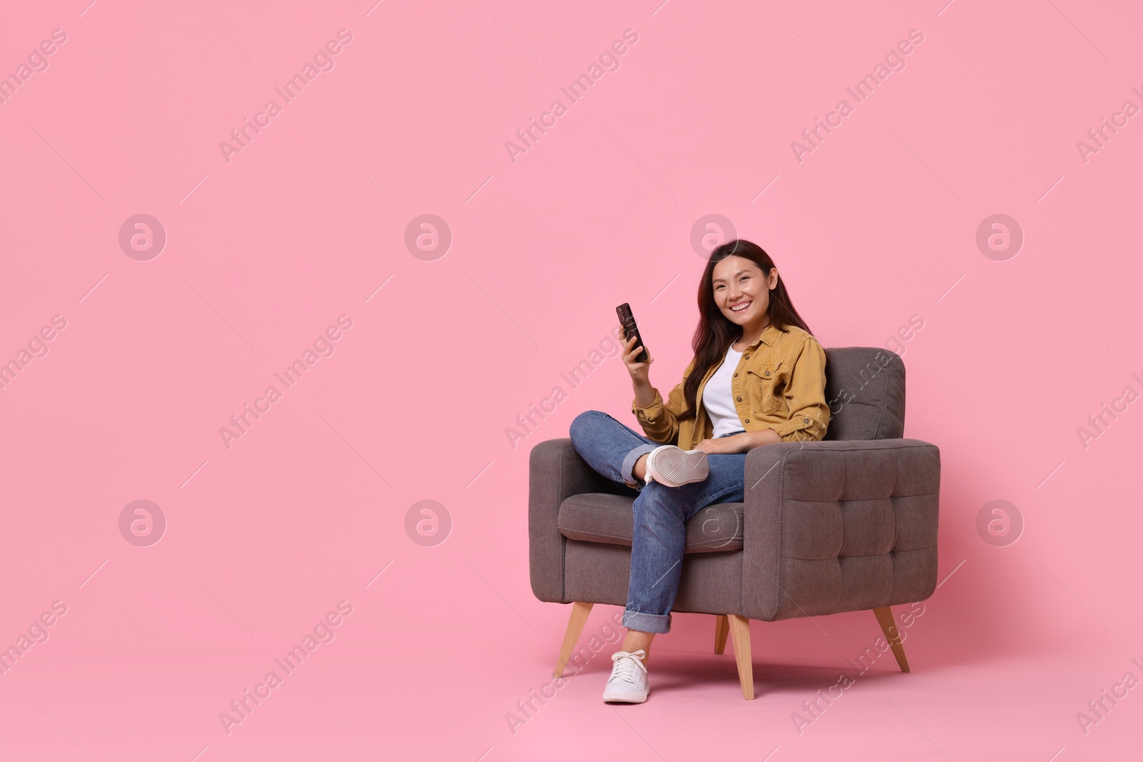 Photo of Smiling woman with smartphone sitting in armchair on pink background. Space for text