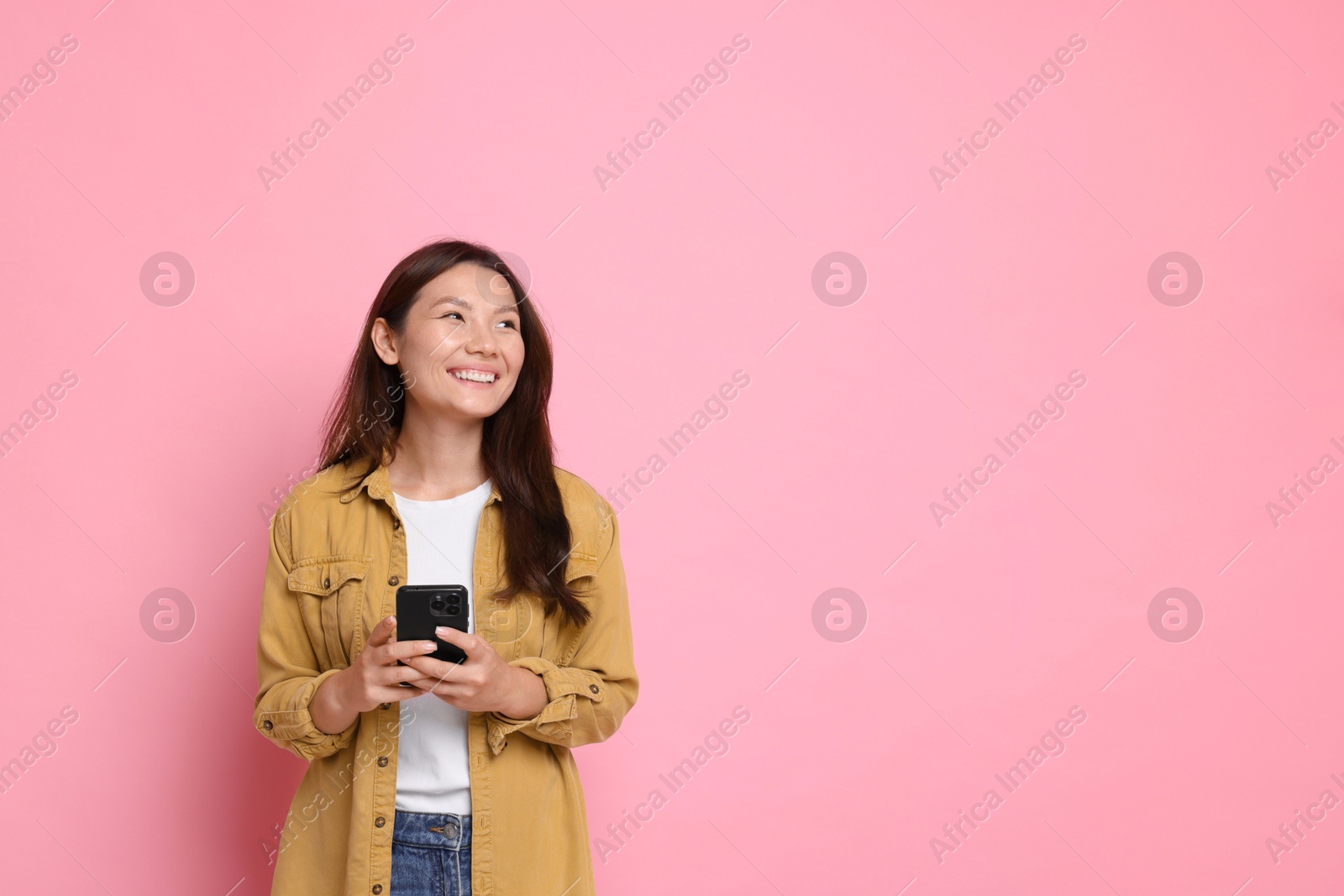 Photo of Smiling young woman with smartphone on pink background. Space for text