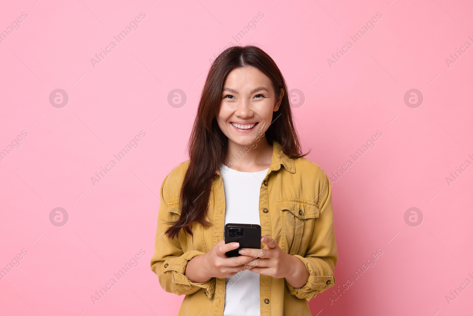 Photo of Smiling young woman with smartphone on pink background