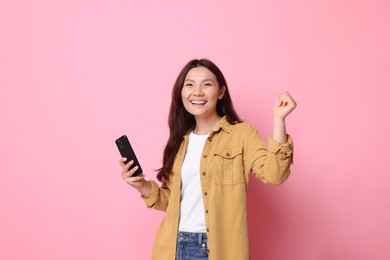 Photo of Smiling young woman with smartphone on pink background