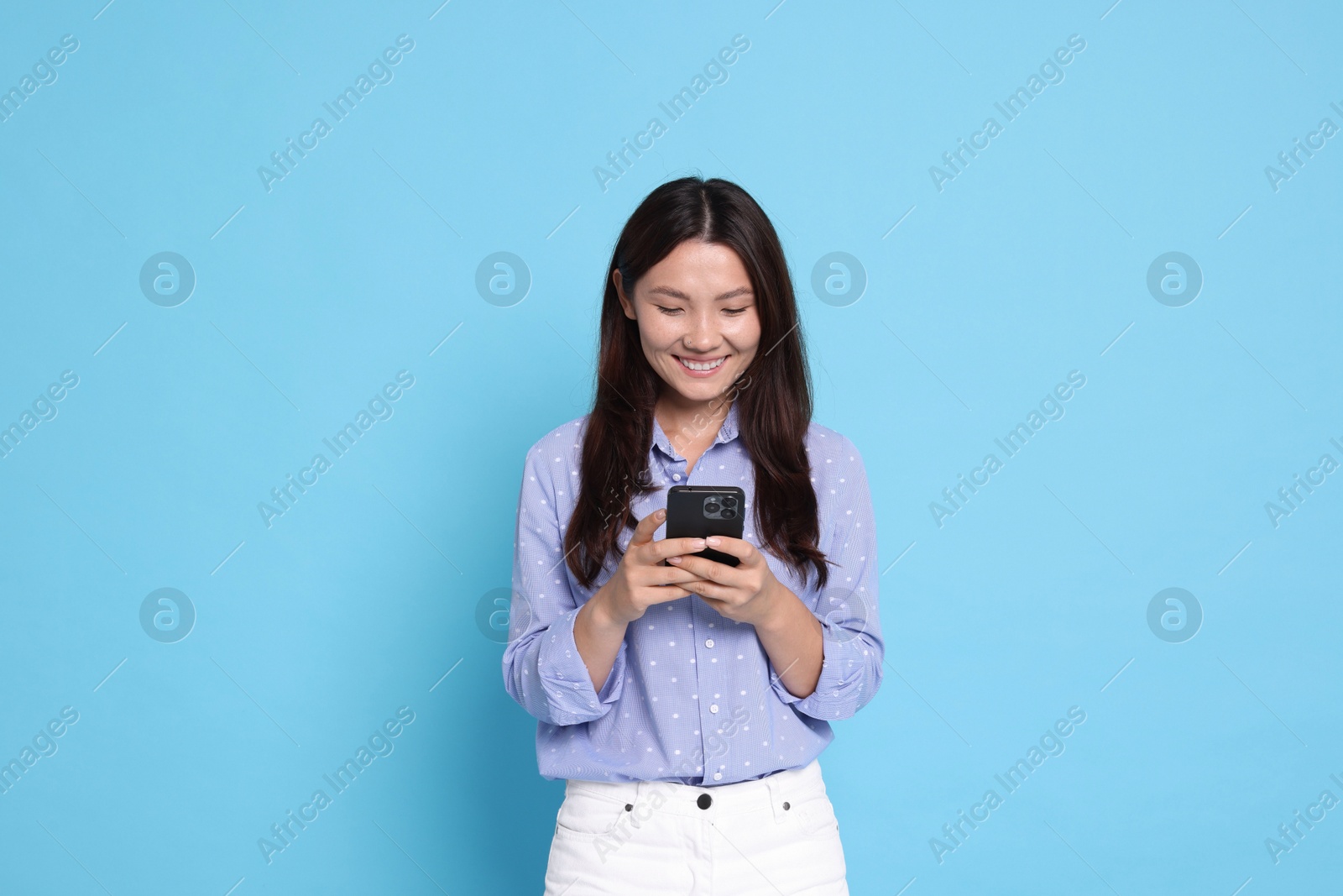 Photo of Smiling woman using smartphone on light blue background